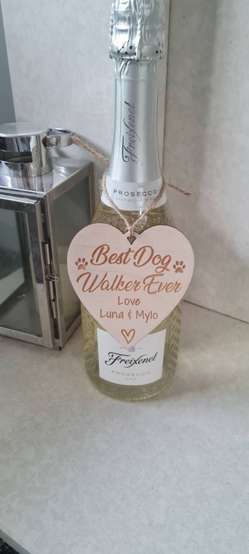 Puede incluir: Un letrero de madera en forma de coraz&oacute;n con el texto "Best Dog Walker Ever" y "Love Luna & Milo" colgado de una botella de Prosecco Freixenet.