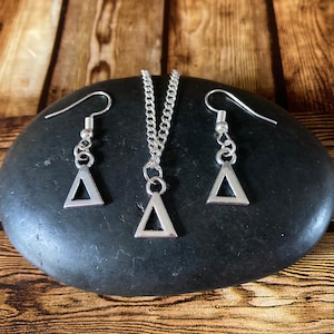 May include: A silver triangle necklace and matching earrings set. The necklace has a delicate chain and a small triangle pendant. The earrings are also small and feature triangle charms.