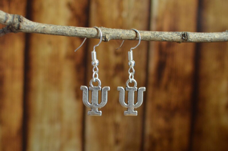 May include: A pair of silver earrings with a Greek letter psi charm hanging from a silver hook.
