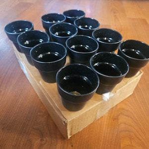 Könnte beinhalten: Eine Sammlung schwarzer Pflanztöpfe aus Kunststoff, angeordnet auf einem Karton. Die Töpfe haben ein einfaches, konisches Design mit glänzendem Finish. Die Töpfe sind leer und bereit zum Bepflanzen.