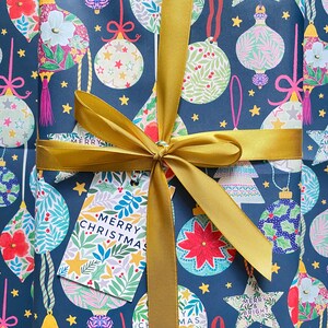 May include: A blue gift wrap with a gold ribbon and a gift tag that says "Merry Christmas". The wrap features a repeating pattern of colorful ornaments, stars, and the words "Merry and Bright".