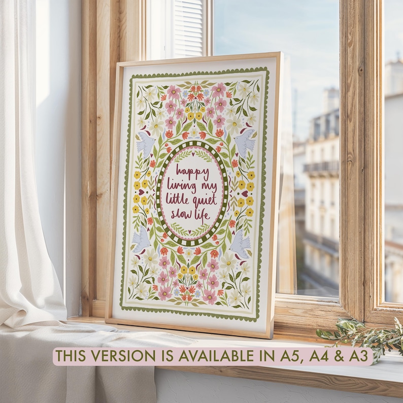 May include: A framed rectangular art print featuring a central oval border containing the text 'happy living my little quiet slow life' in dark red script, surrounded by a symmetrical floral pattern with birds in shades of pink, yellow, and green.