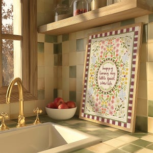 May include: A rectangular framed print featuring a floral border with birds and the text "happy living my little quiet slow life" in the center. The artwork is surrounded by a red and white striped border and set against a tiled kitchen wall.