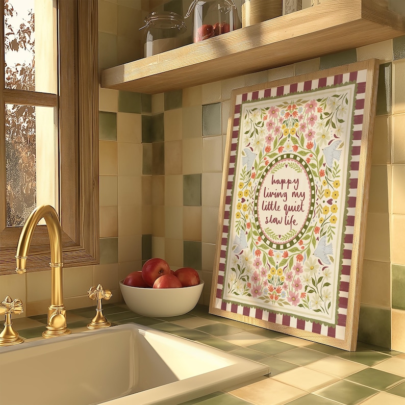 May include: A rectangular framed print featuring a floral border with birds and the text "happy living my little quiet slow life" in the center. The artwork is surrounded by a red and white striped border and set against a tiled kitchen wall.