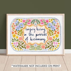 May include: A white framed print with a floral border and the text "enjoy being in the process of becoming". The flowers are in shades of pink, yellow, blue, and green.