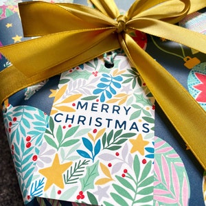 May include: A blue and white gift wrap with a gold ribbon tied in a bow. The gift wrap has a floral pattern with red berries and the gift tag says "Merry Christmas".