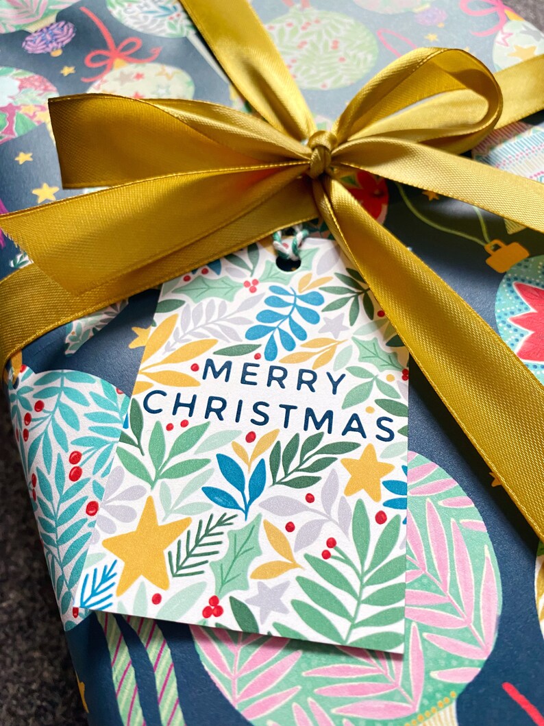 May include: A blue and white gift wrap with a gold ribbon tied in a bow. The gift wrap has a floral pattern with red berries and the gift tag says "Merry Christmas".