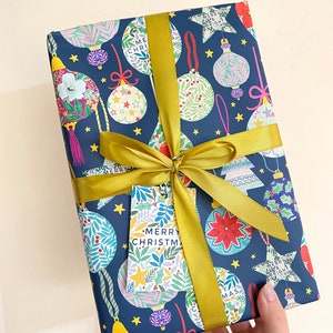 May include: A blue gift wrap with a gold ribbon and a gift tag that says "Merry Christmas". The gift wrap has a pattern of colorful ornaments and stars.