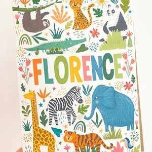 K&ouml;nnte beinhalten: Eine bunte Karte mit dem Namen "FLORENCE" in Regenbogenbuchstaben, umgeben von Dschungeltieren, darunter eine Giraffe, ein Zebra, ein Elefant, ein Tiger, ein Faultier, ein Leopard, ein Panda und ein Krokodil. Die Karte hat einen wei&szlig;en Hintergrund mit gr&uuml;nen, blauen, gelben, orangen, rosa und braunen Akzenten.
