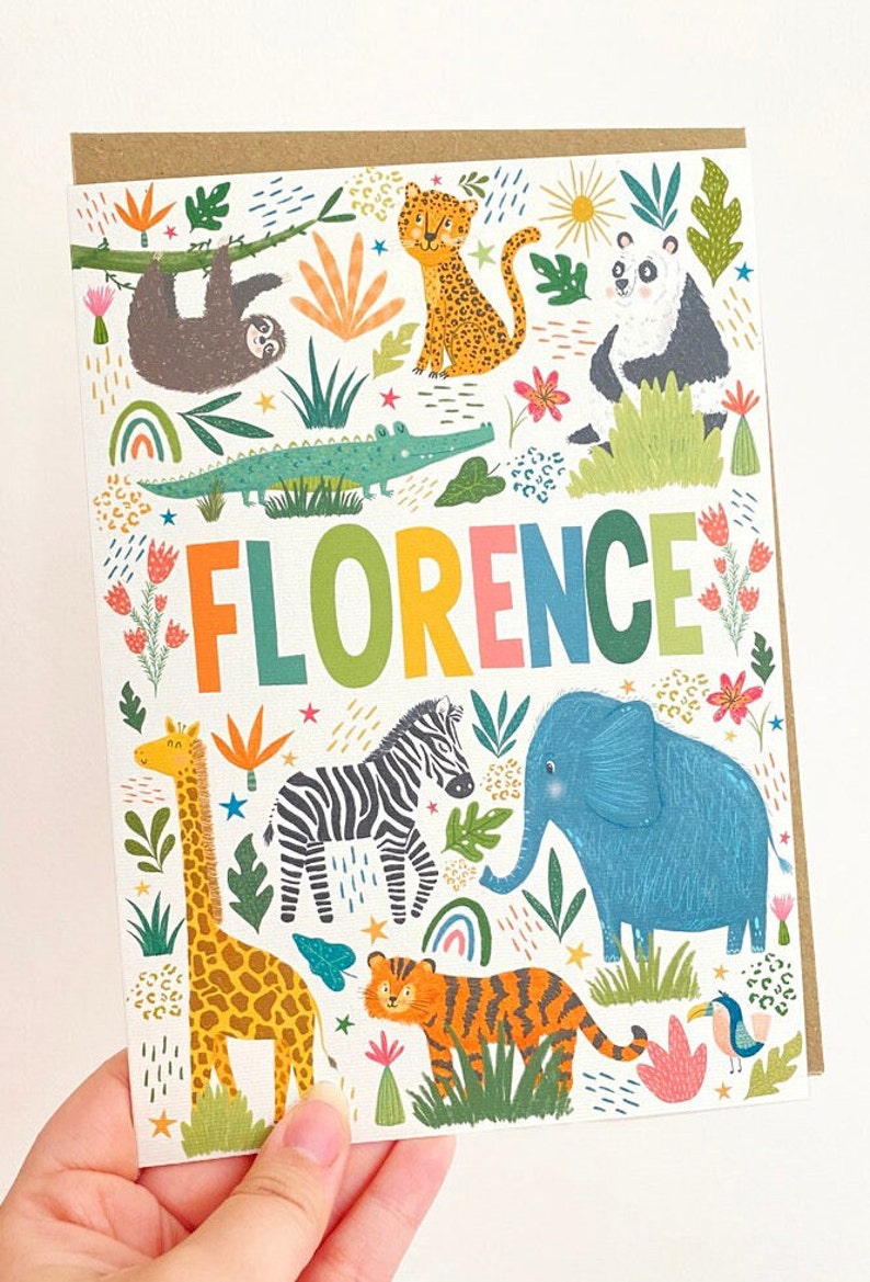 K&ouml;nnte beinhalten: Eine bunte Karte mit dem Namen "FLORENCE" in Regenbogenbuchstaben, umgeben von Dschungeltieren, darunter eine Giraffe, ein Zebra, ein Elefant, ein Tiger, ein Faultier, ein Leopard, ein Panda und ein Krokodil. Die Karte hat einen wei&szlig;en Hintergrund mit gr&uuml;nen, blauen, gelben, orangen, rosa und braunen Akzenten.