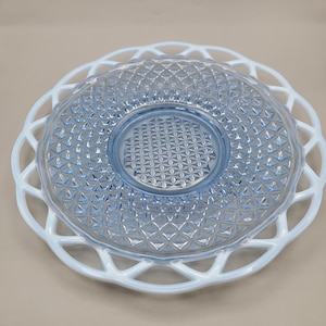 May include: A two-tiered serving dish. The top tier is a light blue glass plate with a diamond pattern. The bottom tier is a white, openwork, lace-like plate. The plates are designed for serving food.