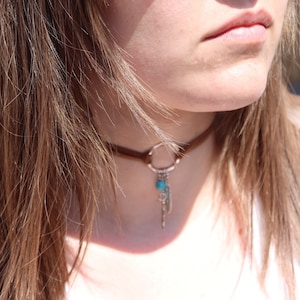 May include: A brown suede choker necklace with a silver circle pendant and a turquoise bead charm.