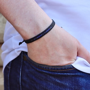 May include: A black braided bracelet with a thin blue stripe woven into the design.
