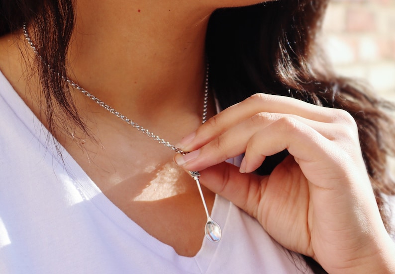 May include: A silver chain necklace with a small, oval-shaped pendant. The pendant is a spoon.