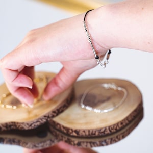 Peut inclure: Un bracelet en argent avec des perles et un cordon noir, ainsi qu'un fermoir en argent. Le bracelet est sur un présentoir en bois.