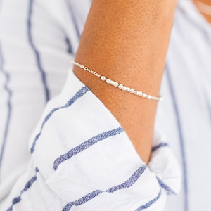 May include: A silver beaded bracelet with a delicate chain. The bracelet is on a person's wrist.