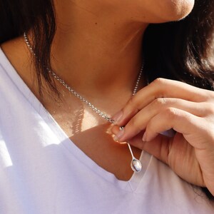 May include: A silver chain necklace with a small, oval-shaped pendant. The pendant is a spoon.