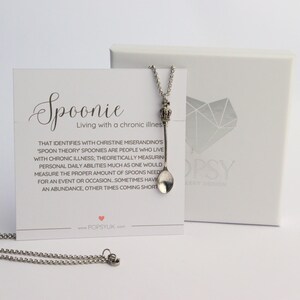 May include: A silver spoon necklace with a small crown charm. The necklace is on a white card with the text "Spoonie Living with a chronic illness" and a definition of the term "Spoonie".