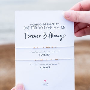 May include: A white card with the text "Morse Code Bracelet One for You One for Me Forever & Always" and the words "Forever" and "Always" written in Morse code below. The card is held by a hand.