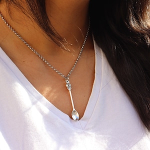 May include: A silver chain necklace with a spoon pendant. The spoon has a crown-shaped top and a rounded bowl.