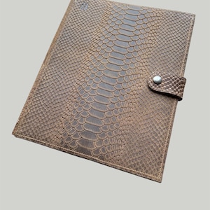 Puede incluir: Una carpeta de cuero marrón con un patrón de piel de serpiente y un cierre de botón plateado.