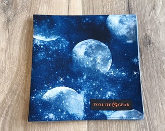 May include: A blue cotton handkerchief with a white moon and stars pattern. The handkerchief has a black label with the text "Foxlite Gear" in white.