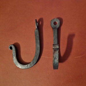 May include: Two black metal hooks with a simple design. The hooks are made of forged metal and have a rustic look.
