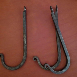 Puede incluir: Tres ganchos de metal negro con un rizo decorativo en la parte superior. Los ganchos están hechos de hierro forjado y tienen un acabado rústico.