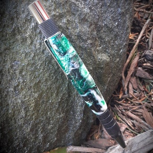May include: A black and green pen with a silver top and a textured black grip. The pen has a swirling green and white pattern.