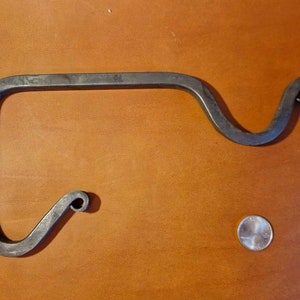 May include: A black metal hook with a unique curved design. The hook is about 10 inches long and has a diameter of about 1/2 inch. It is shown on a brown surface.