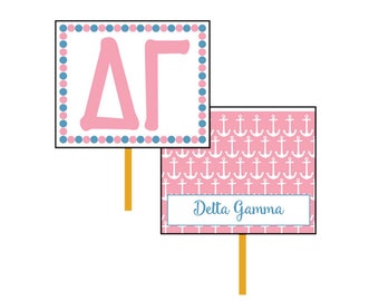May include: Two pink and white signs with a nautical anchor pattern. The top sign has a blue and pink polka dot border and the letters Delta Gamma in pink. The bottom sign has the text "Delta Gamma" in blue.