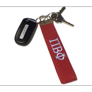 May include: A red fabric key fob with the Greek letters ΠΒΦ embroidered in light blue. The fob is attached to a set of keys and a black Jeep key fob.