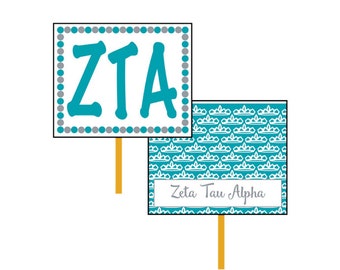 May include: Two teal blue and white signs with a stick attached to the bottom. The top sign has a white background with a gray dotted border and the letters "ZTA" in teal blue. The bottom sign has a teal blue background with a white crown pattern and the text "Zeta Tau Alpha" in white.