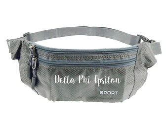 May include: Gray fanny pack with two zippered compartments and an adjustable strap. The text "Delta Phi Epsilon SPORT" is printed on the front. The bag is made of a textured material and has a gray buckle.