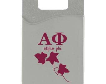 May include: A gray phone wallet with a slot for cards. The wallet features the Greek letters ΑΦ in burgundy, with the words "alpha phi" below. Burgundy ivy leaves are also displayed.