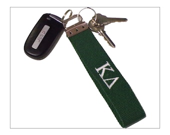 May include: A dark green fabric keychain with the embroidered letters "KΔ" in white. The keychain is attached to a car key fob with the "Jeep" logo and two metal keys.