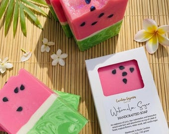 May include: Handmade watermelon-shaped soap bars with pink, green, and white layers. The soap has black seed details and glitter accents. A box of soap is also visible, with the text "Watermelon Sugar HANDCRAFTED SOAP".