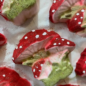 May include: A set of five bath bombs shaped like mushrooms. The bath bombs are pink, green, and red with white polka dots. They are covered in glitter.