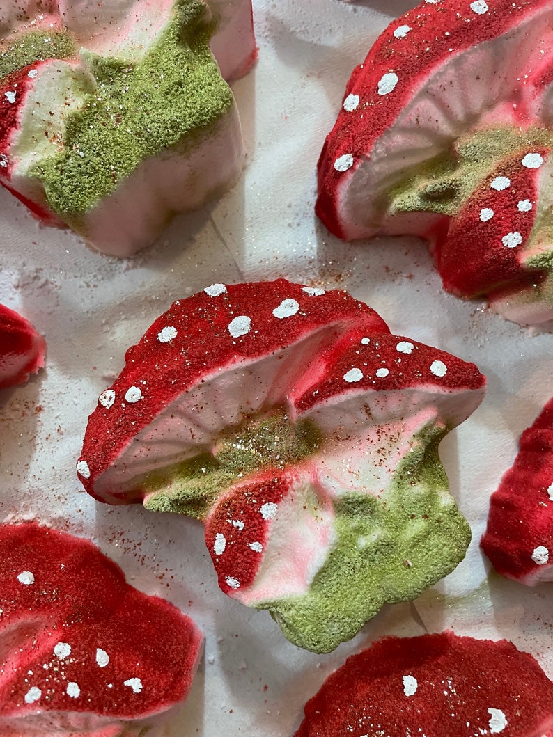 May include: A set of five bath bombs shaped like mushrooms. The bath bombs are pink, green, and red with white polka dots. They are covered in glitter.