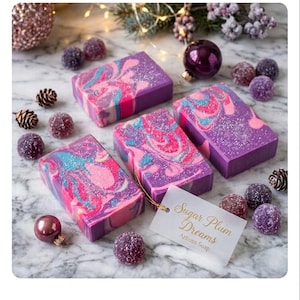 May include: Four rectangular bars of artisan soap with a swirl of pink, blue, and white on a purple base. The soap is surrounded by decorative ornaments, pinecones, and candies. A tag reads "Sugar Plum Dreams Artisan Soap."