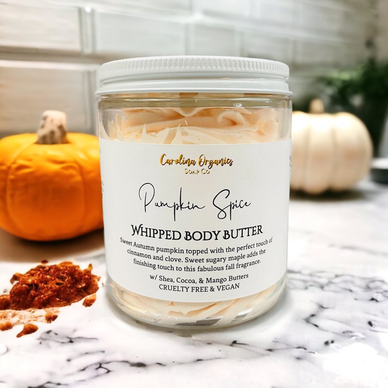 May include: A glass jar of whipped body butter with a white lid. The jar is labeled "Carolina Organics Soap Co. Pumpkin Spice Whipped Body Butter". The label also says "Sweet Autumn pumpkin topped with the perfect touch of cinnamon and clove. Sweet sugary maple adds the finishing touch to this fabulous fall fragrance. w/ Shea, Cocoa, & Mango Butters Cruelty Free & Vegan."