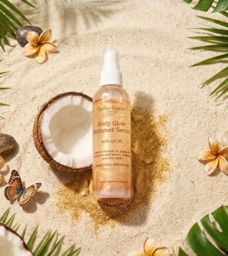 May include: A bottle of Body Glow Shimmer Serum with SPF 20, on a sandy surface with a halved coconut, flowers, and a butterfly. The bottle has a white spray top and a label with product information.