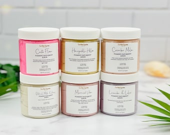 May include: Six jars of foaming face and body scrub with various scents, including Cactus Flower, Honeysuckle Hills, Cucumber Melon, Oatmeal Milk & Honey, Mermaid Vibe, and Lavender & Lilac. Each jar has a white lid and a label with the name of the scent and the words "Foaming Face & Body Scrub".