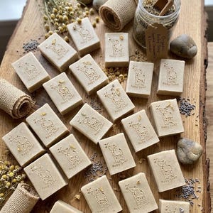 Puede incluir: Jabones rectangulares para beb&eacute;s con un dise&ntilde;o de jirafa y la inscripci&oacute;n "Baby Soap". Los jabones est&aacute;n dispuestos sobre una tabla de madera, junto con flores secas, un tarro de hierbas y peque&ntilde;as piedras. Cada jab&oacute;n mide unos 6 cm.