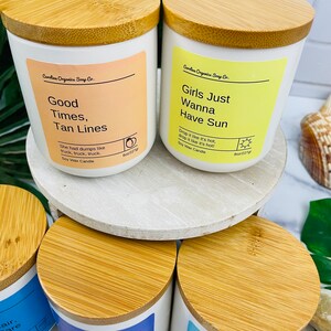 Puede incluir: Cuatro velas de cera de soja blancas con tapas de madera. Las velas est&aacute;n etiquetadas con frases veraniegas: "Good Times, Tan Lines", "Girls Just Wanna Have Sun", "Happiness Vibes", y "High Tides, Good Vibes".