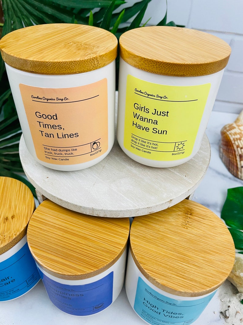 Puede incluir: Cuatro velas de cera de soja blancas con tapas de madera. Las velas est&aacute;n etiquetadas con frases veraniegas: "Good Times, Tan Lines", "Girls Just Wanna Have Sun", "Happiness Vibes", y "High Tides, Good Vibes".