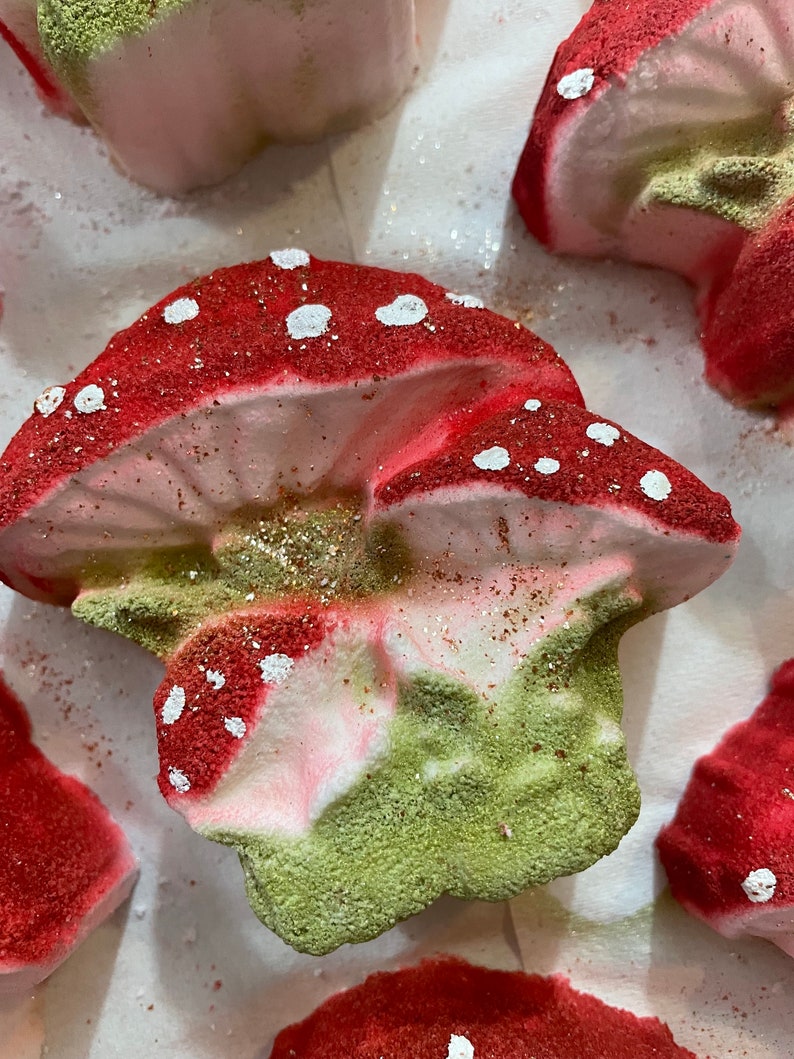 May include: A set of bath bombs shaped like mushrooms. The mushrooms are red and white with green accents. The bath bombs are covered in glitter.
