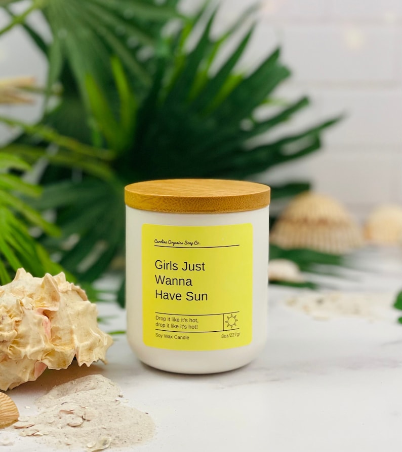 Puede incluir: Una vela de cera de soja blanca con una tapa de madera. La vela est&aacute; etiquetada "Girls Just Wanna Have Sun" y tiene un icono de sol. La vela es de 8 oz/227g.