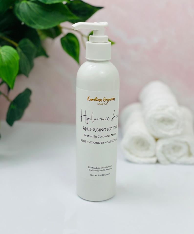 May include: White bottle of Hyaluronic Acid Anti-Aging Lotion with a pump dispenser. The bottle is labeled with the text "Carolina Organics Soap Co." and "Scented in Cucumber Melon".