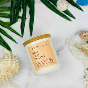 Puede incluir: Vela de cera de soja blanca con tapa de bamb&uacute;. La etiqueta dice "Good Times, Tan Lines" y "She had dumps like truck, truck, truck". La vela es de 8 oz/227g.